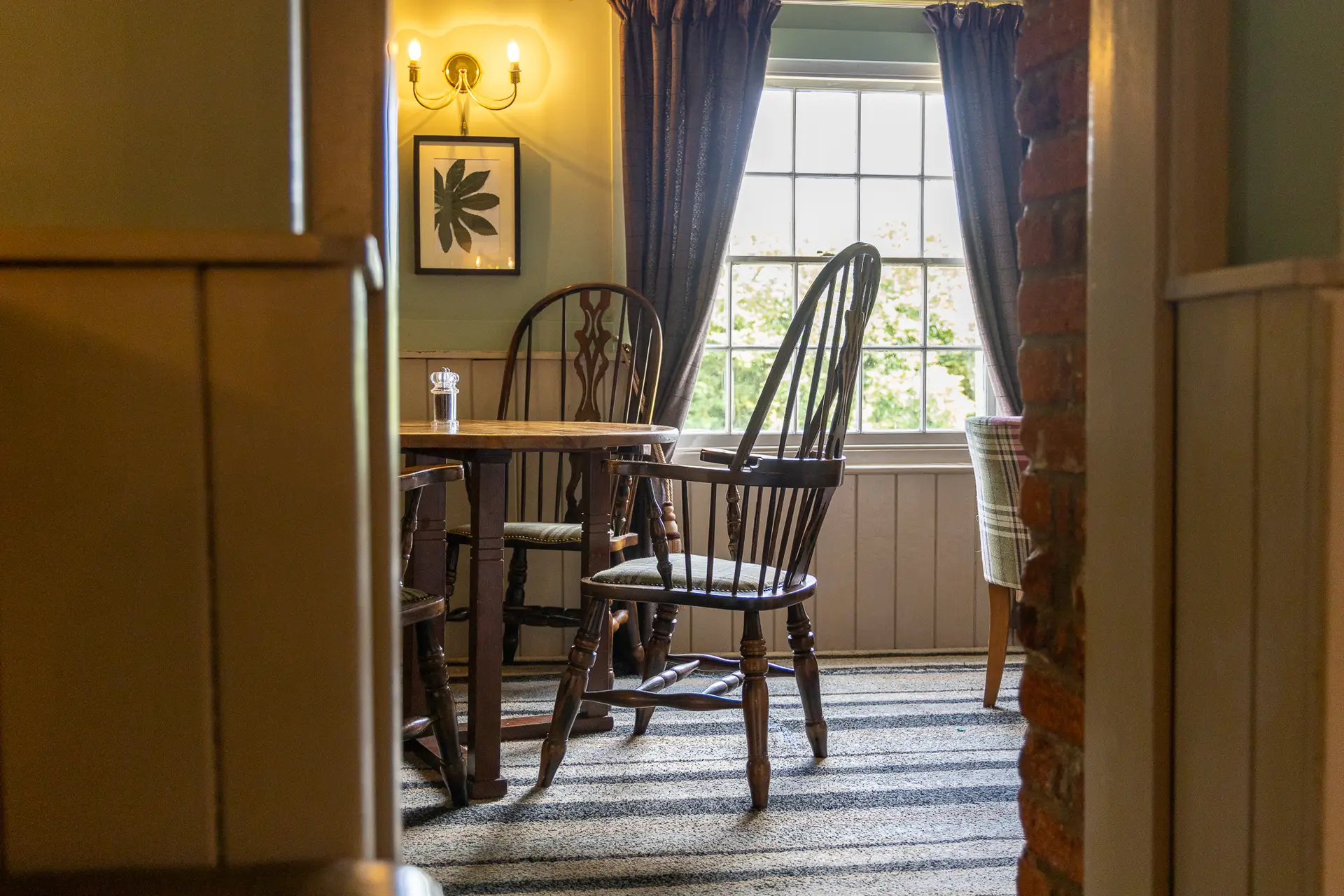 Wooden dining chair and table beside a sunlit window at The Old Red Lion, Horseheath