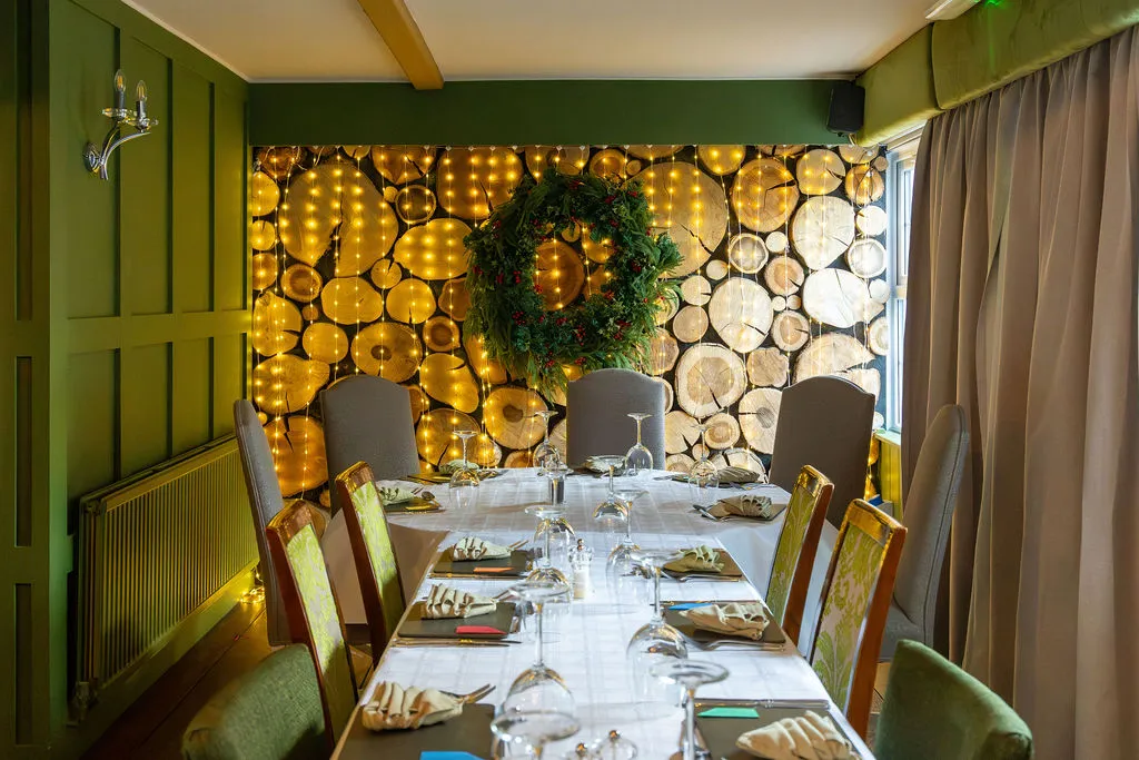 Table laid for Christmas dining beneath a lit wreath at The Old Red Lion, Horseheath