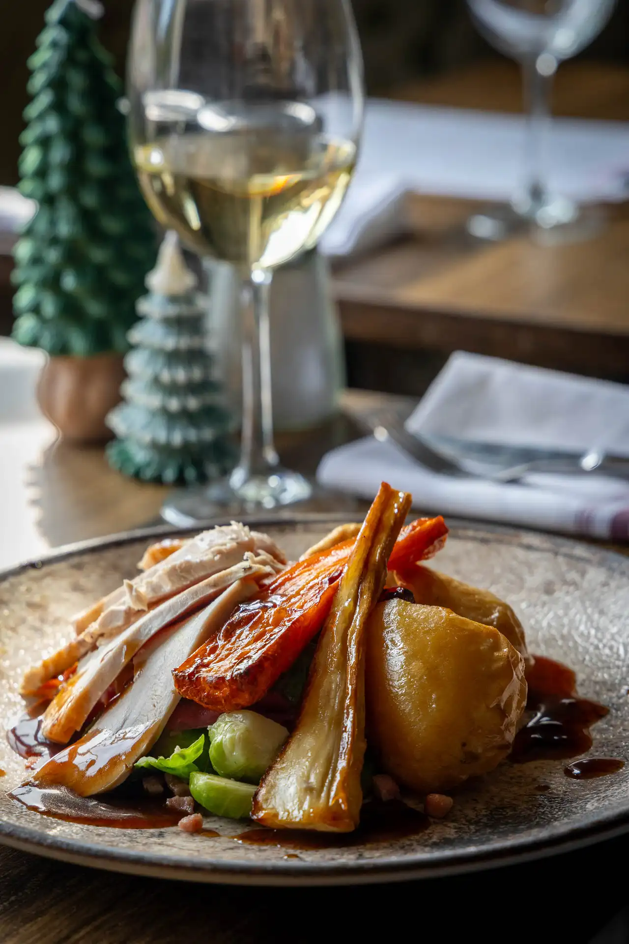 Butter Roasted Essex, Grove Smith Turkey with duck fat potatoes, honey roasted carrots & parsnips and rich gravy, with white wine and small Christmas trees on the table, at The Old Red Lion, Horseheath