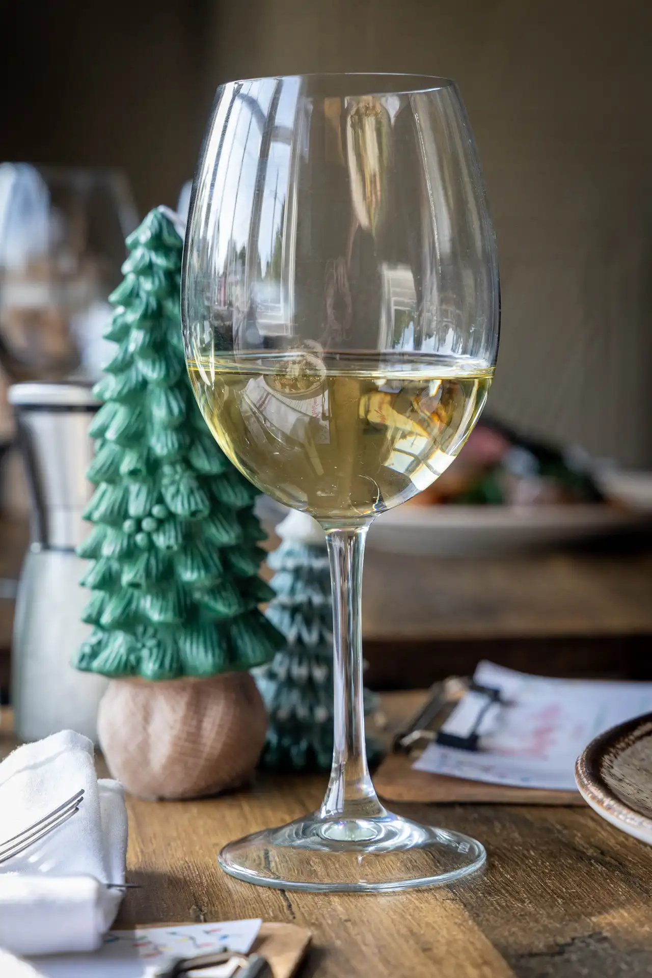 A glass of white wine on a wooden table beside green Christmas tree decorations, at The Old Red Lion, Horseheath